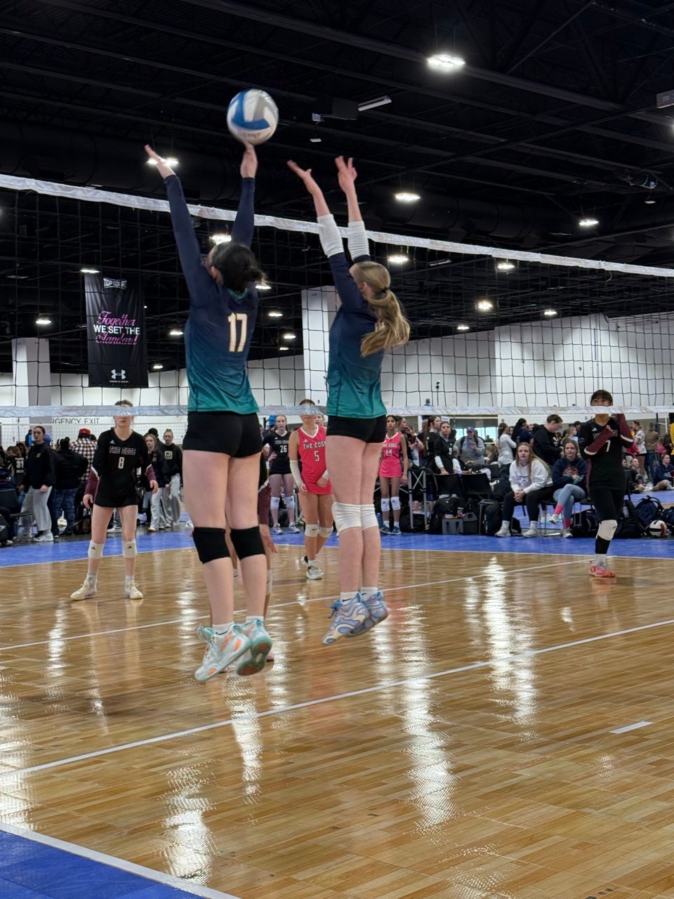 Two female volleyball players in action jumping high to block a ball.